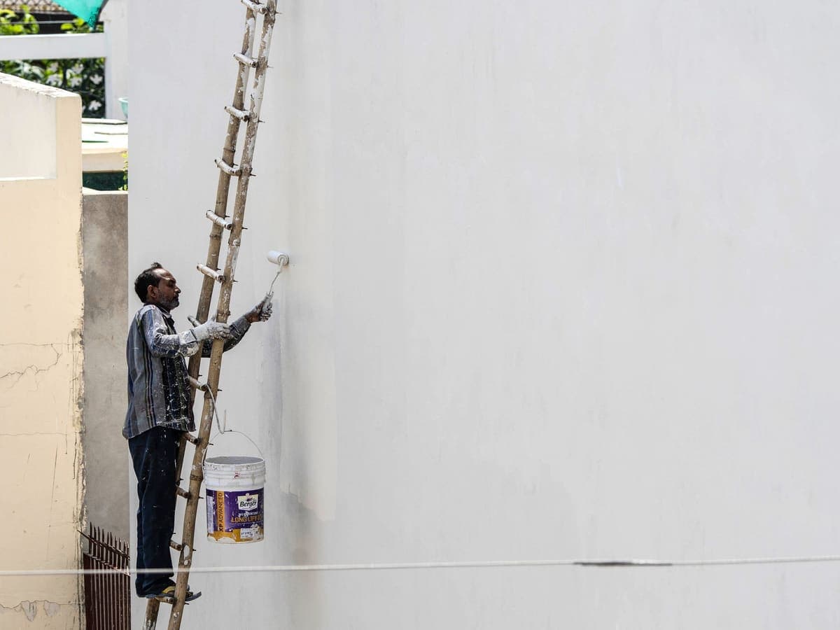 Peintre en façade appliquant une peinture claire au rouleau
